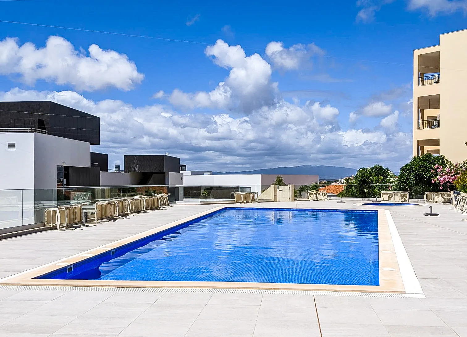 An outdoor swimming pool is surrounded by a paved deck and seating.