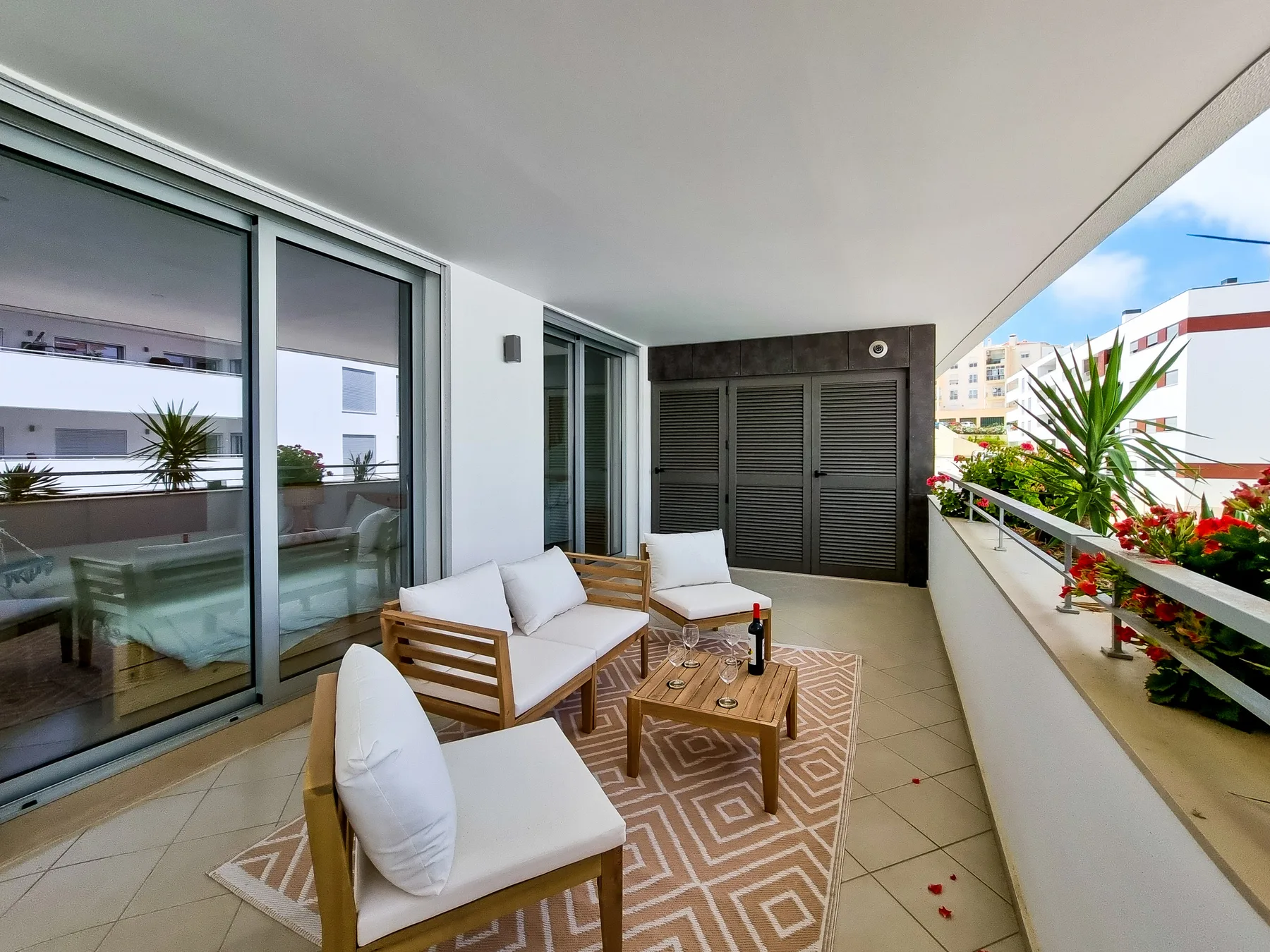 A furnished balcony with seating, a small table, and potted plants.