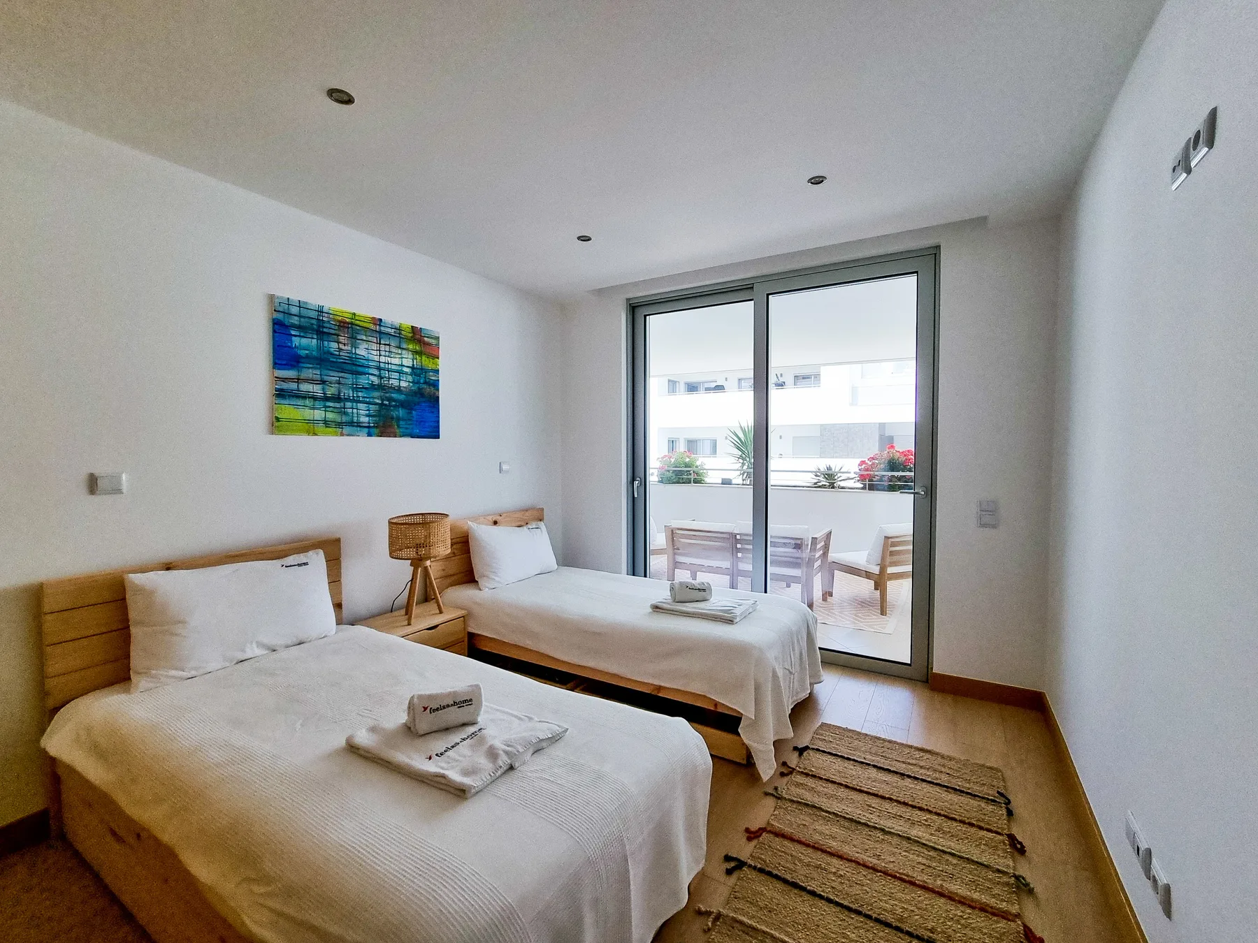 A bright bedroom with two beds and glass doors opening onto a terrace.