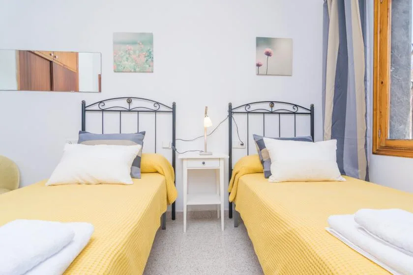 A bedroom with two single beds, a small bedside table, and yellow bedding.