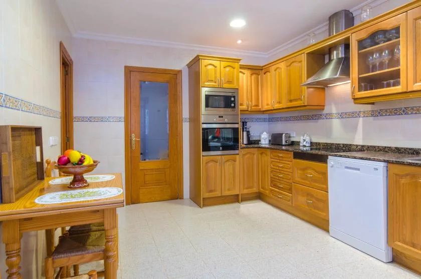A kitchen with wooden cabinetry, built-in appliances, and a small table.
