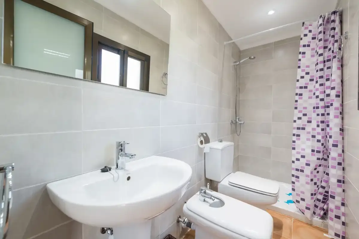 A tiled bathroom with a sink, toilet, and patterned shower curtain.