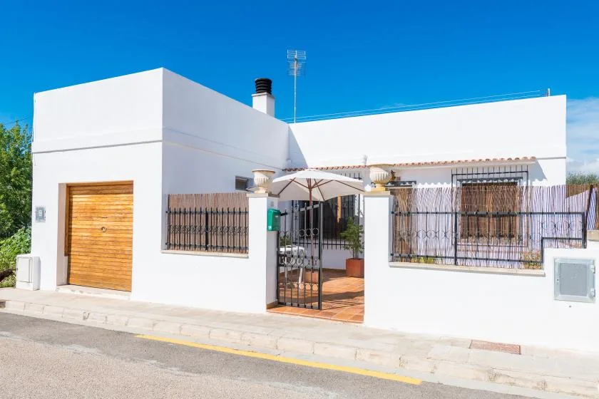 A white modern house stands behind a low wall and black metal gate.