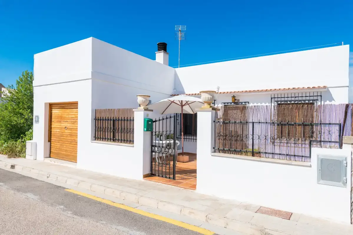 A white modern house faces the street, with barred windows and a wooden door.