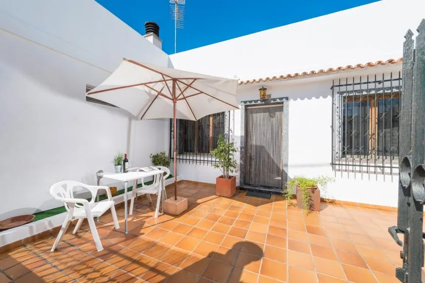 A sunny tiled patio with outdoor seating beneath a large umbrella.