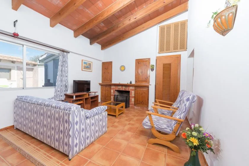 A living room with patterned seating, a television, and exposed wooden ceiling beams.