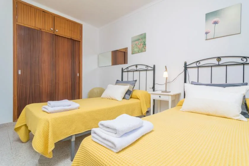 A bedroom with two yellow-covered beds and folded towels.