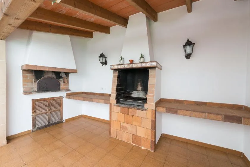 A tiled indoor cooking area with two brick fireplaces and wooden ceiling beams.