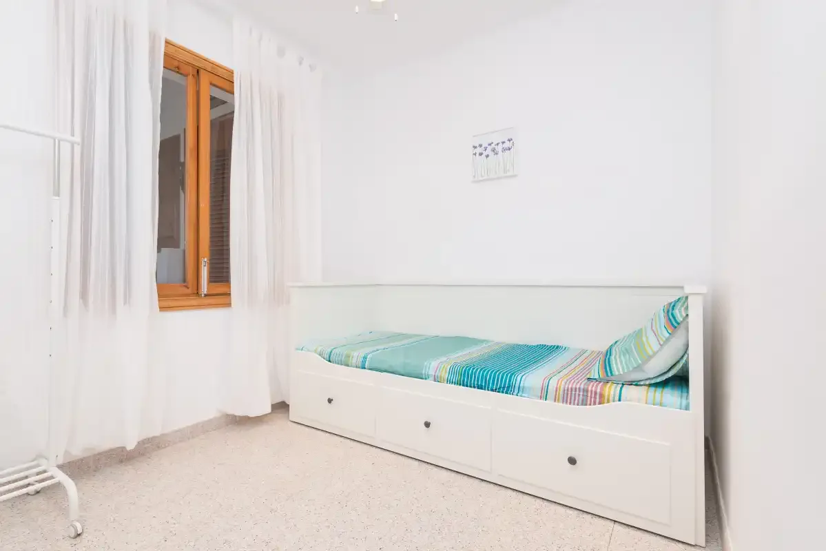 A bright bedroom with a single bed and white curtains.