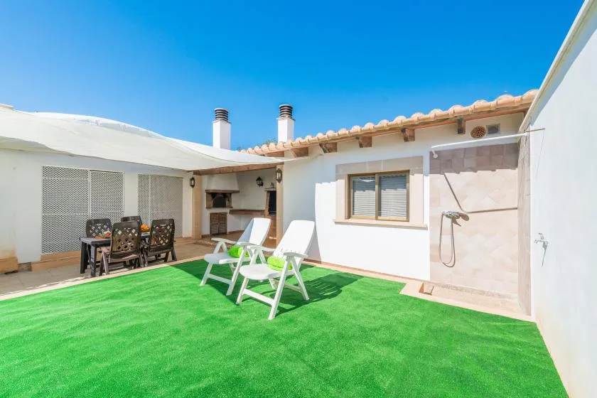 A sunny outdoor patio with artificial grass, seating, and a wall-mounted shower.