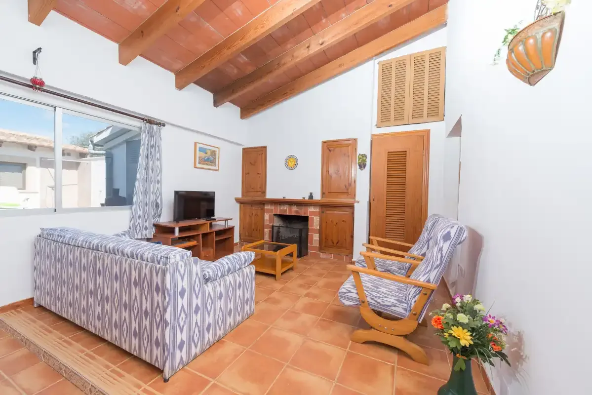 A living room with patterned seating, a television, and exposed wooden ceiling beams.