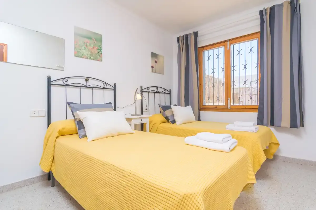 A bedroom with two yellow-covered beds beside a window.