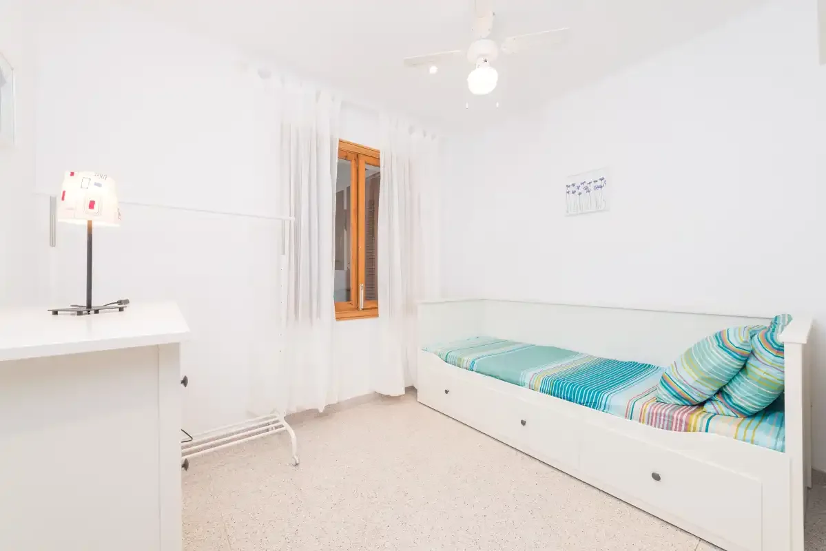 A bright bedroom with a single bed, desk, and curtained window.