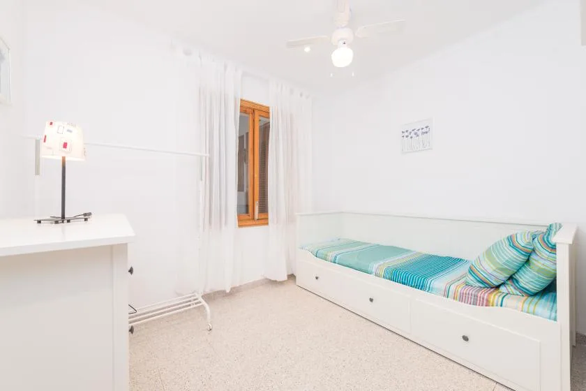 A bright bedroom with a single bed beneath a window.