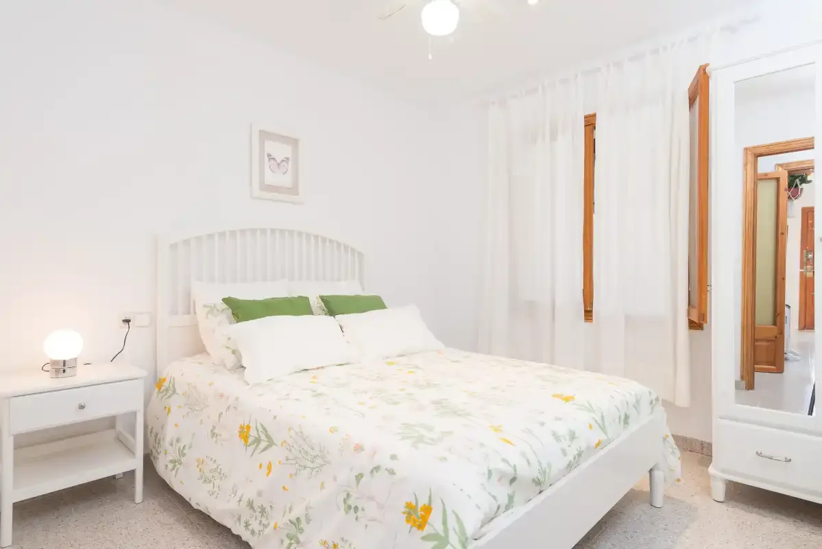 A bright bedroom with a white bed and floral bedding.