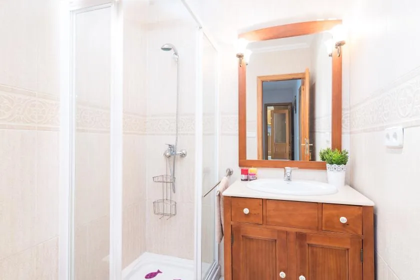 A bright bathroom with a glass shower and a wooden vanity beneath a mirror.