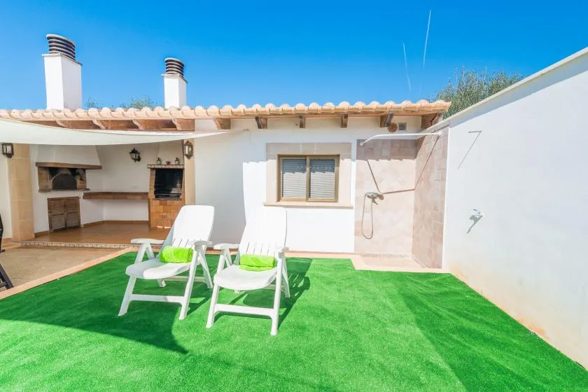 A sunny patio with white lounge chairs on green artificial turf.