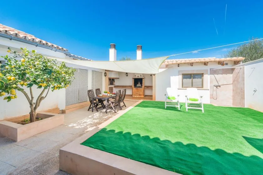 A sunny patio with outdoor seating, a grill, and a green lawn.