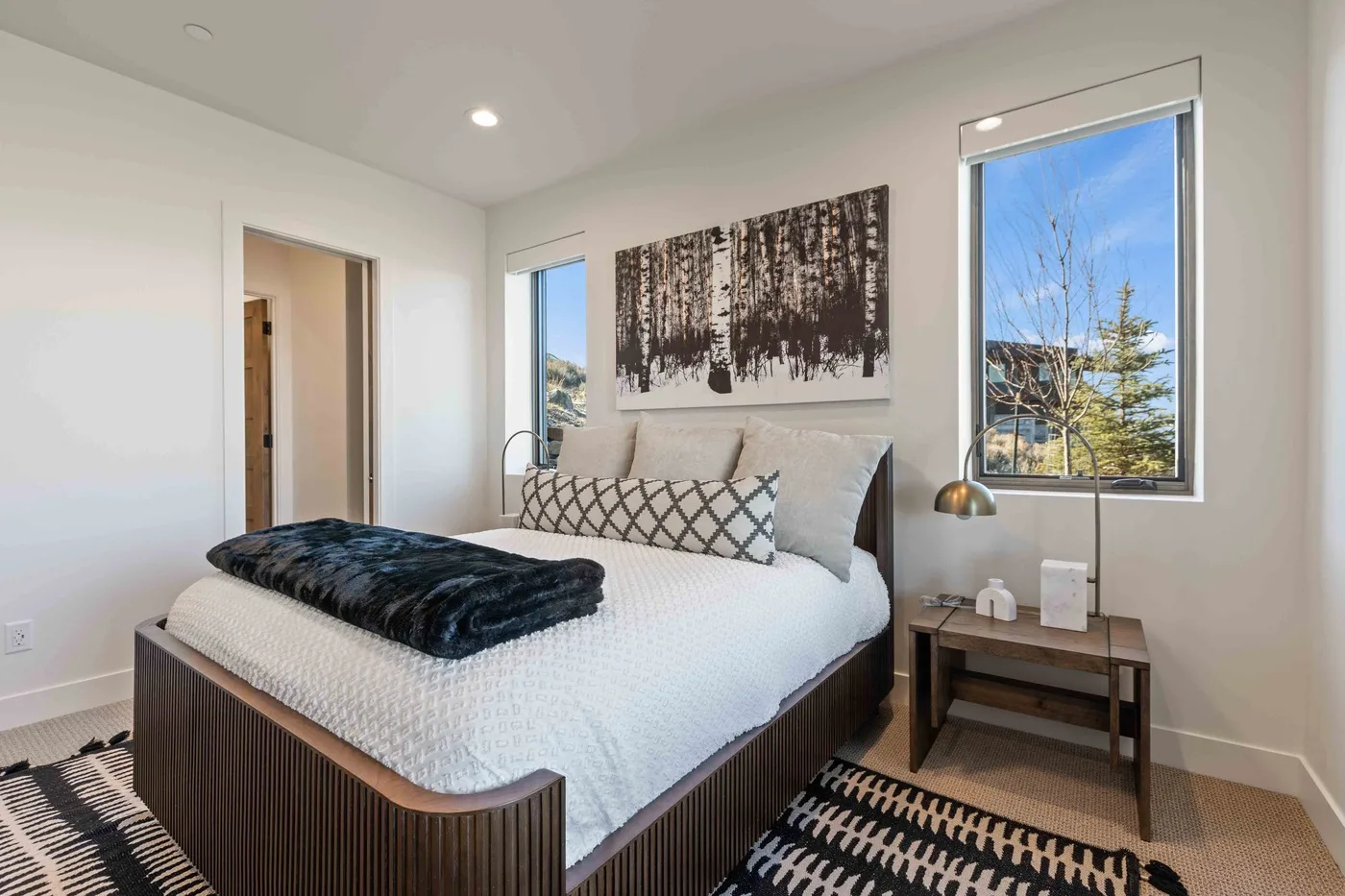 A bright bedroom with a bed beneath a large forest-themed artwork.