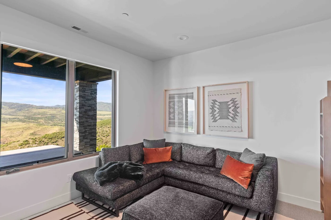 A bright living room with a dark sectional seating area beside large windows.