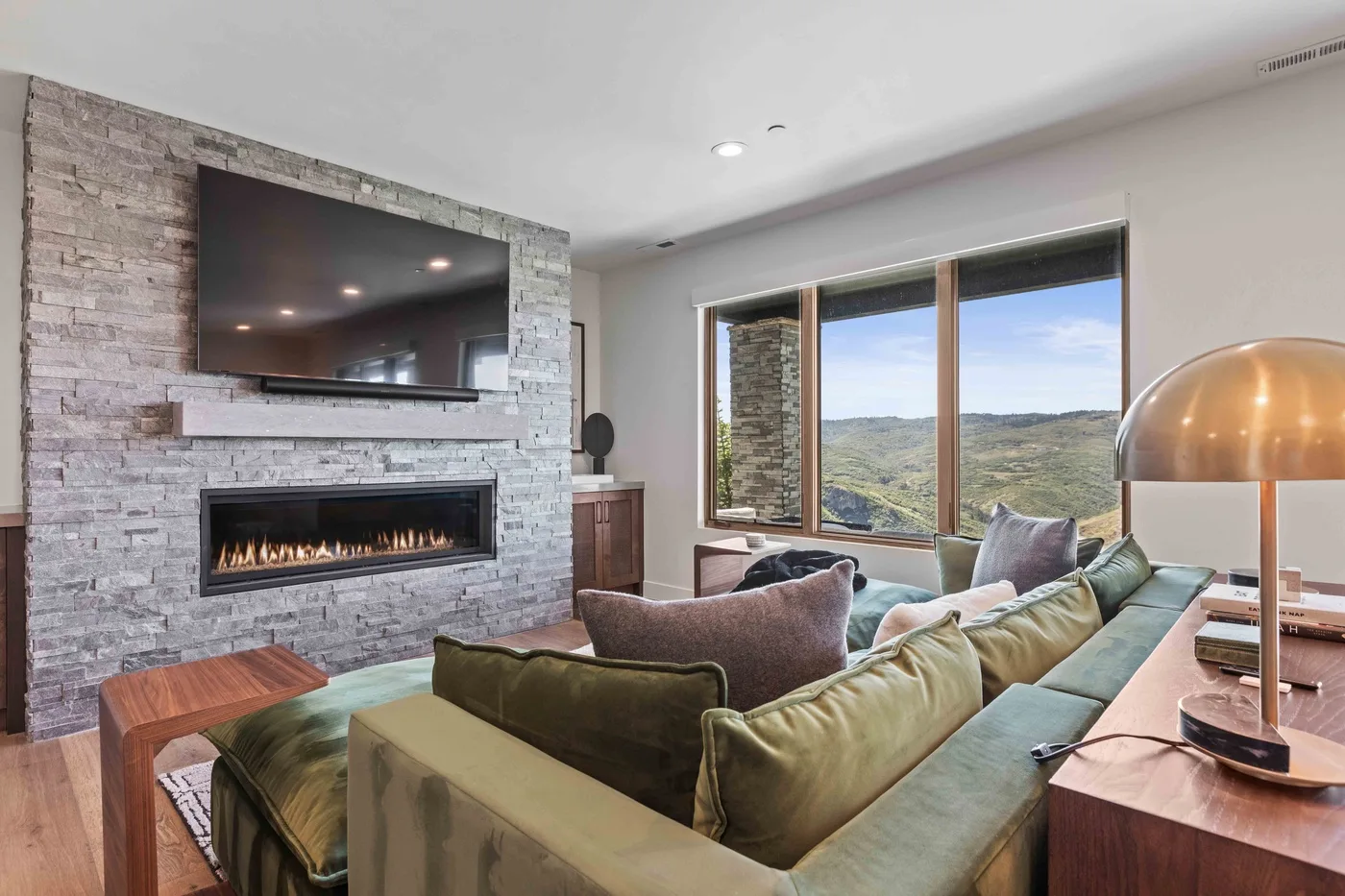 A living room with seating facing a stone fireplace and large windows.