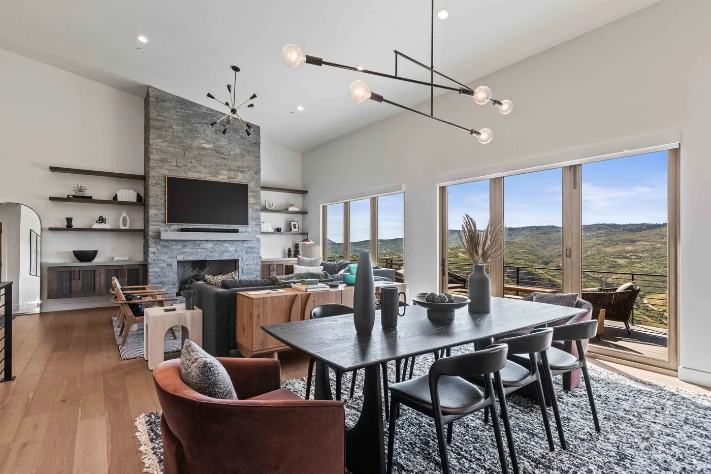 A dining and living area with a long table and large windows overlooking hills.