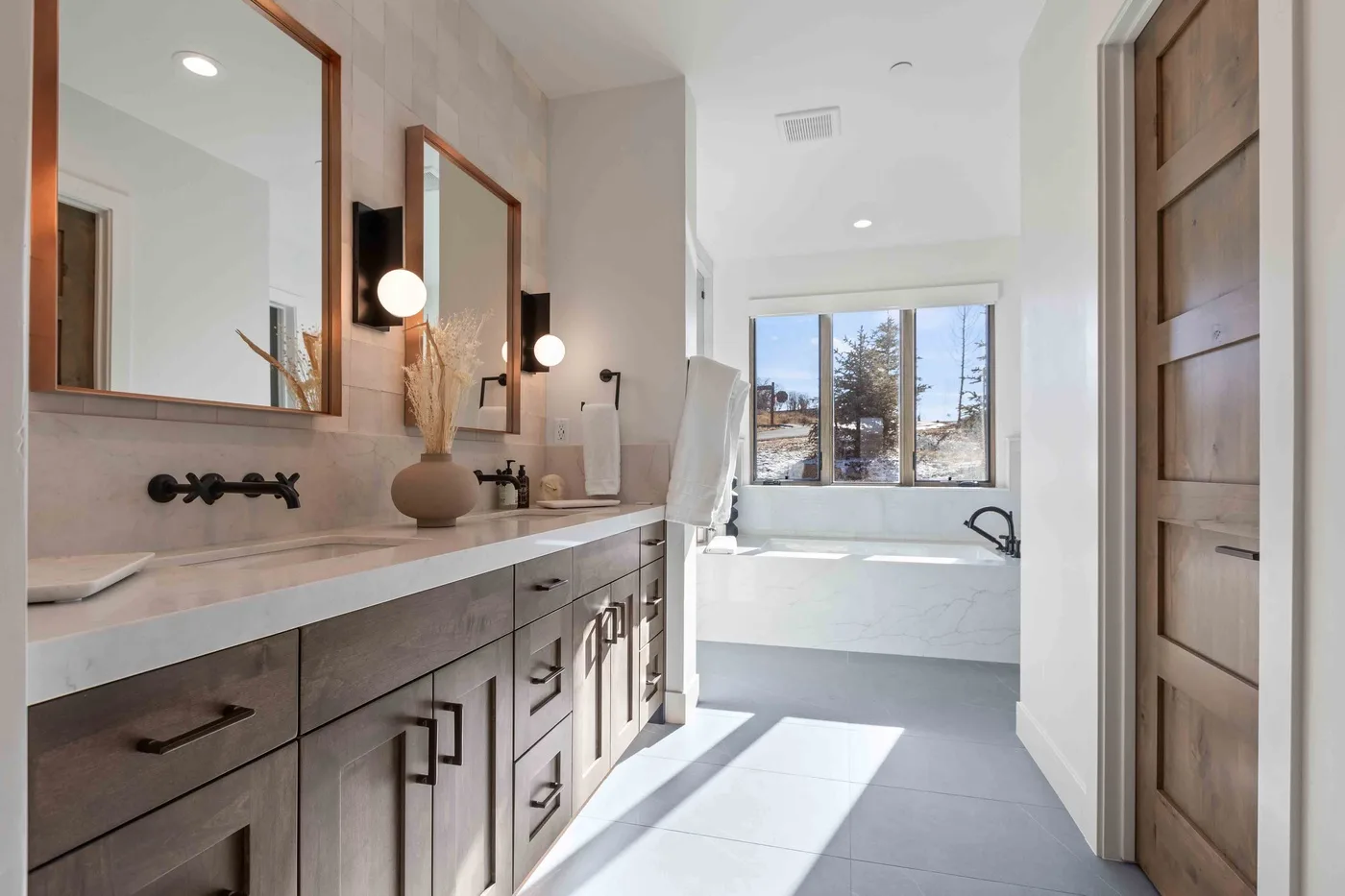 A bright bathroom has a long vanity and a bathtub beneath a window.