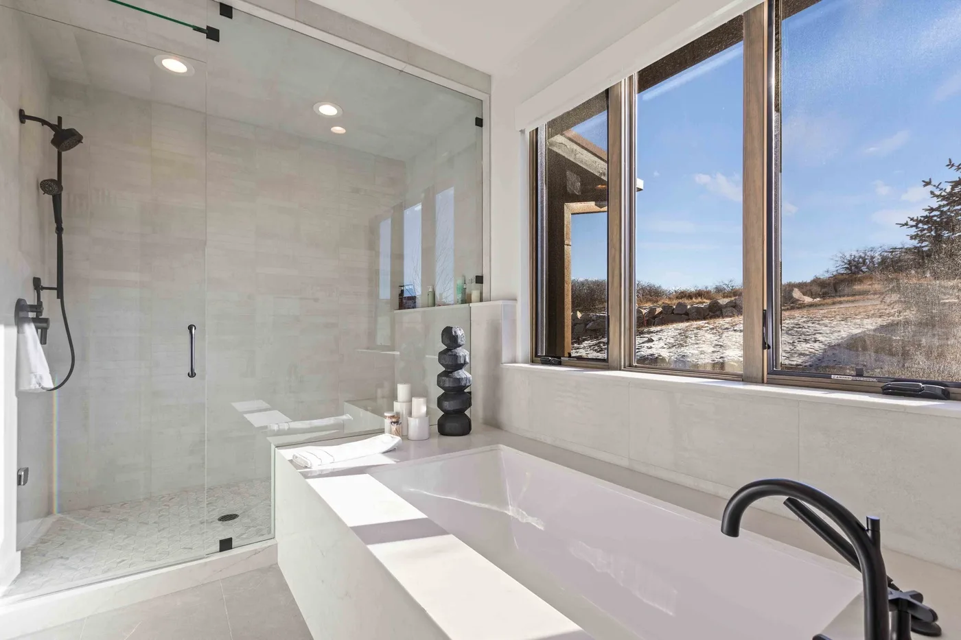 A bright bathroom with a glass shower, a bathtub, and large windows.