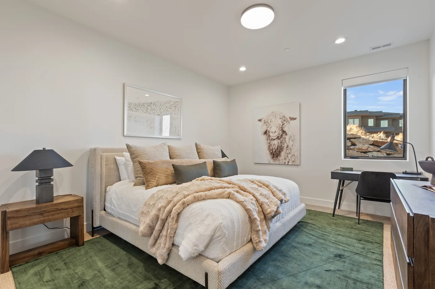 A bright bedroom with a bed, green rug, and a large window.