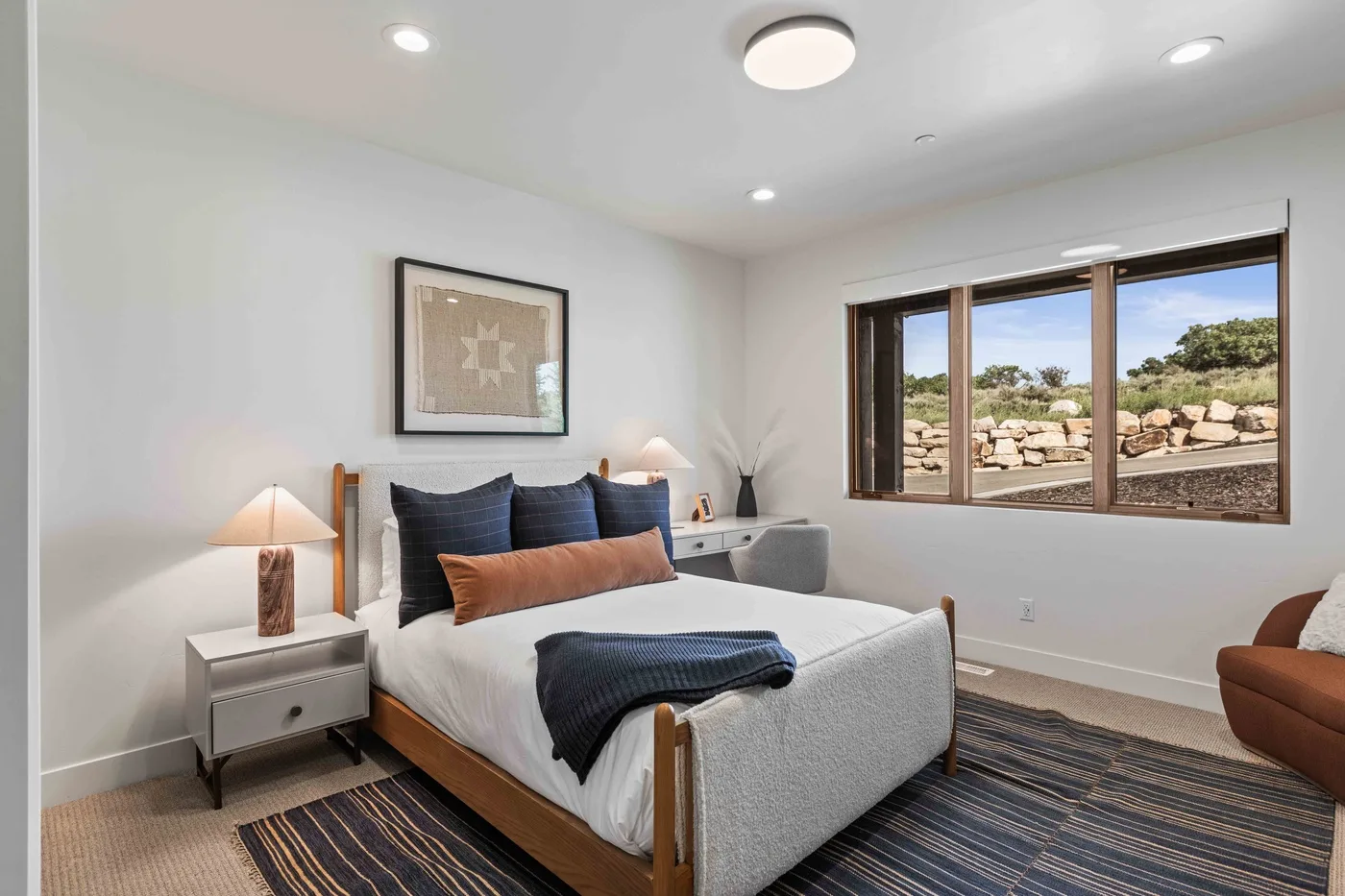 A bedroom with a bed beneath framed wall art and a large window.