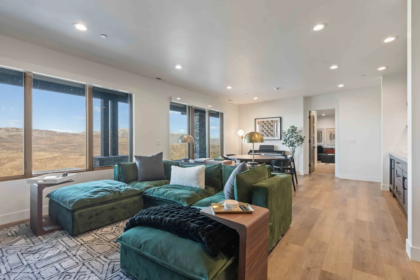 A bright living room with green seating, large windows, and a wooden floor.