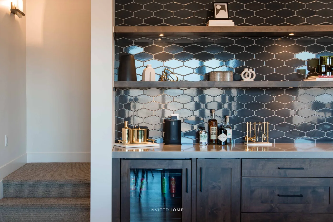 A kitchenette with dark hexagonal tile backsplash and open shelves of small appliances.