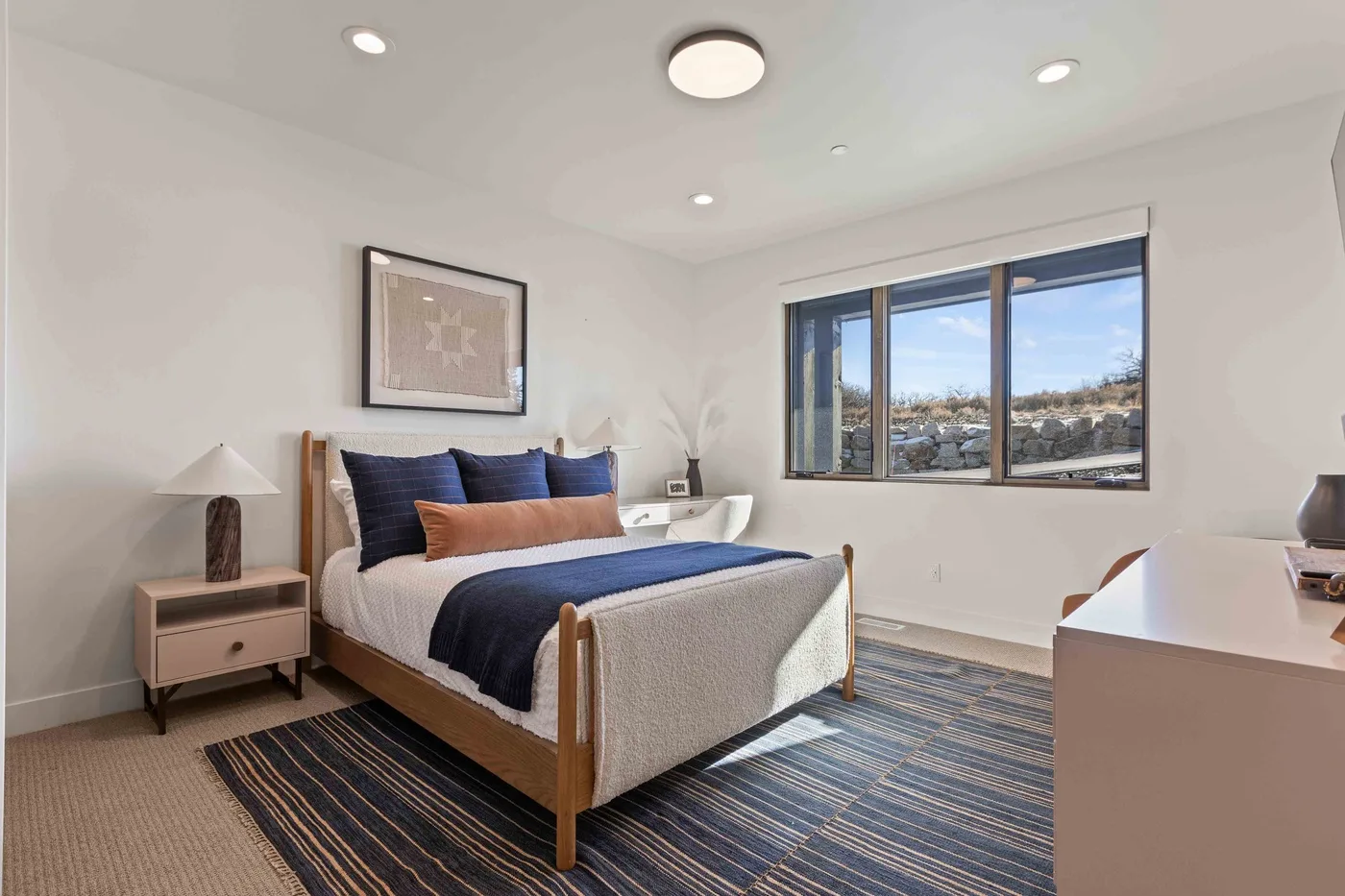 A bedroom with a bed beside a large window overlooking the surrounding landscape.