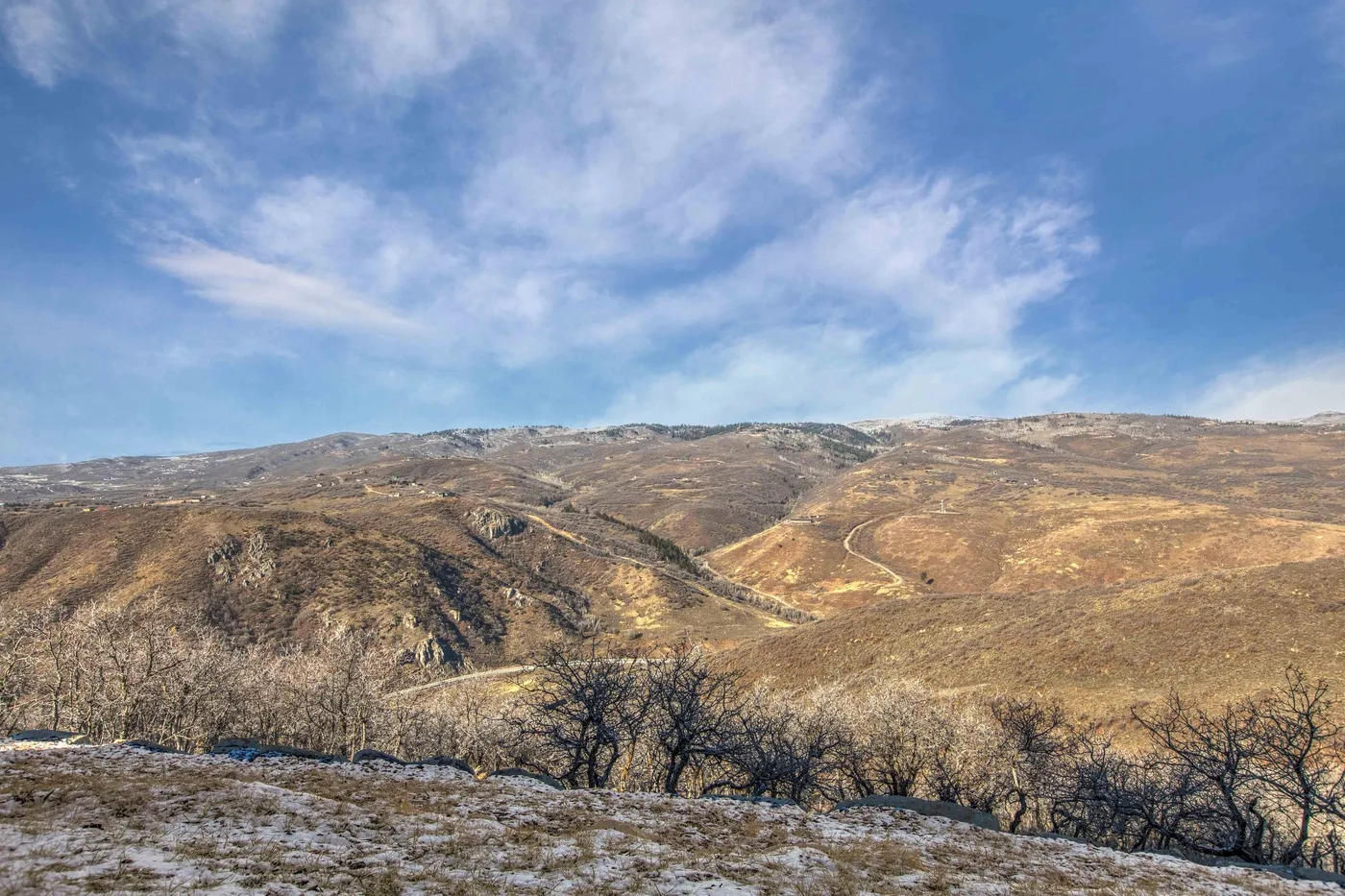 A broad view of dry rolling hills beneath a partly cloudy sky.