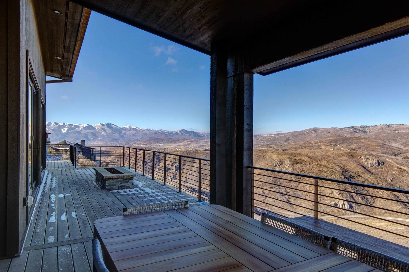 A covered outdoor deck with wooden seating overlooks a wide, dry mountain landscape.