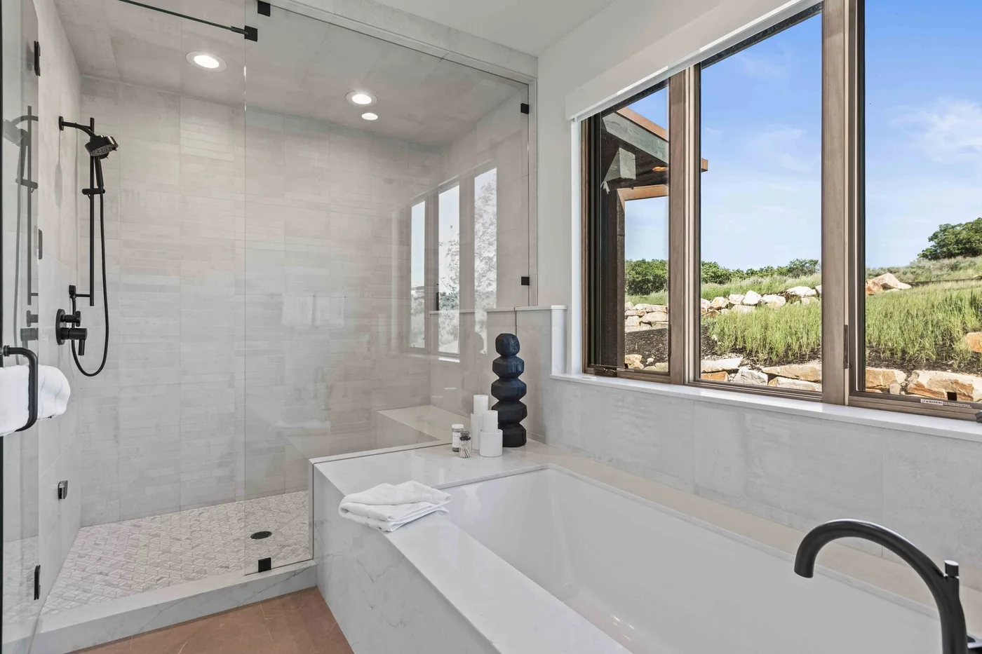 A bright bathroom with a bathtub, shower, and large windows overlooking greenery.