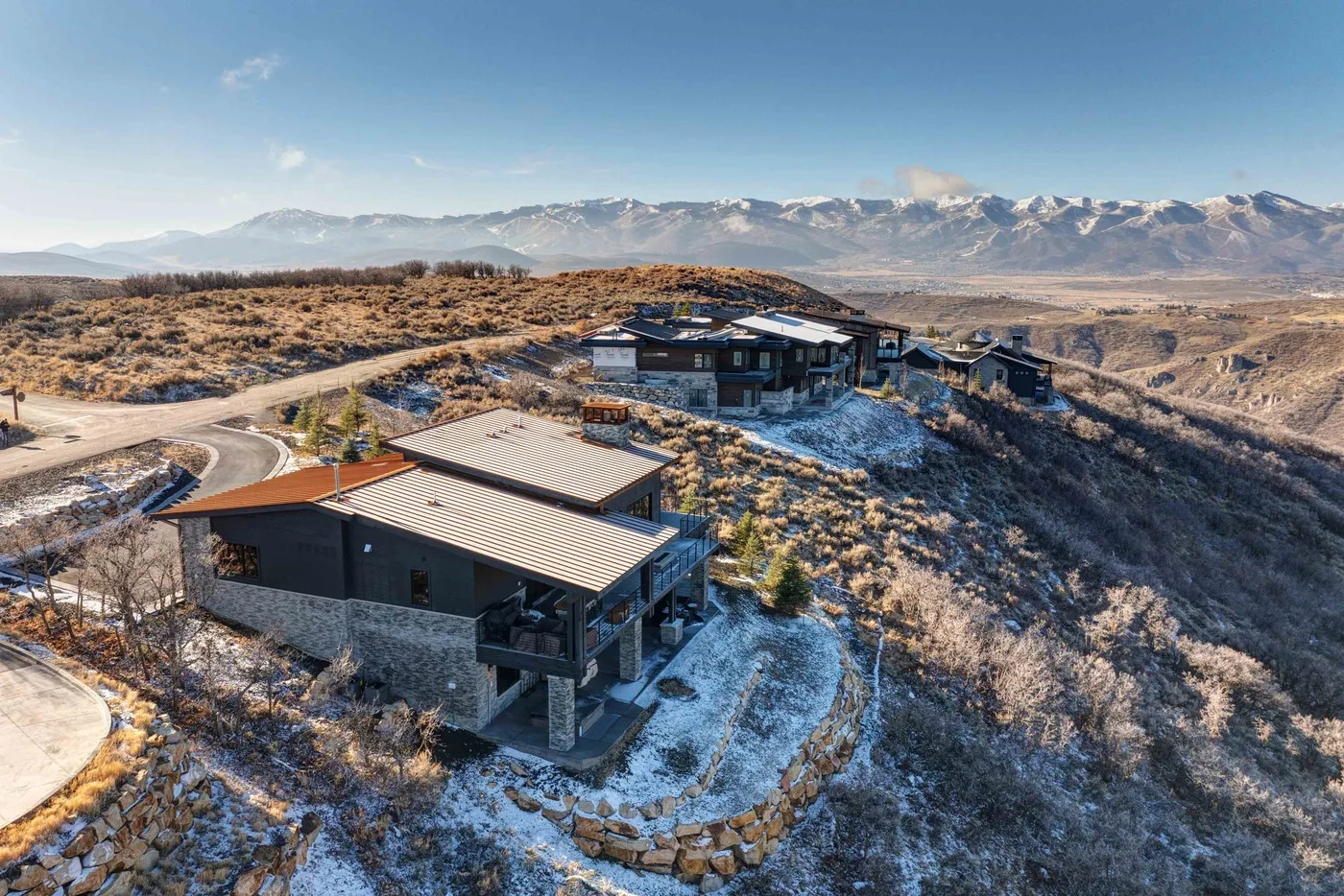 Aerial view of modern homes along a winding road in a snow-dusted mountain landscape.