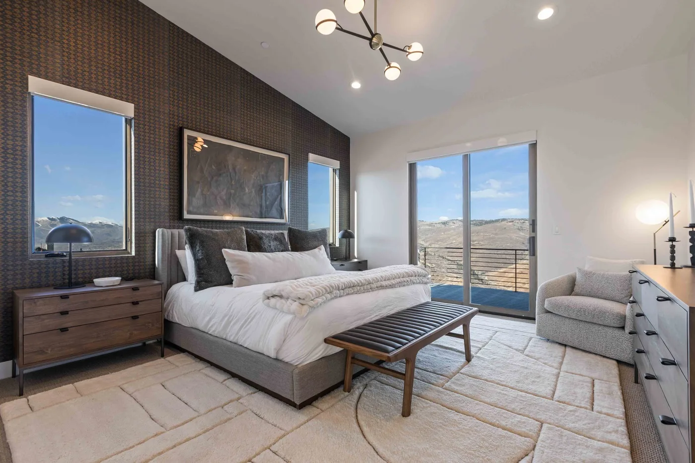 A bedroom with a bed, a bench, and large windows overlooking the landscape.