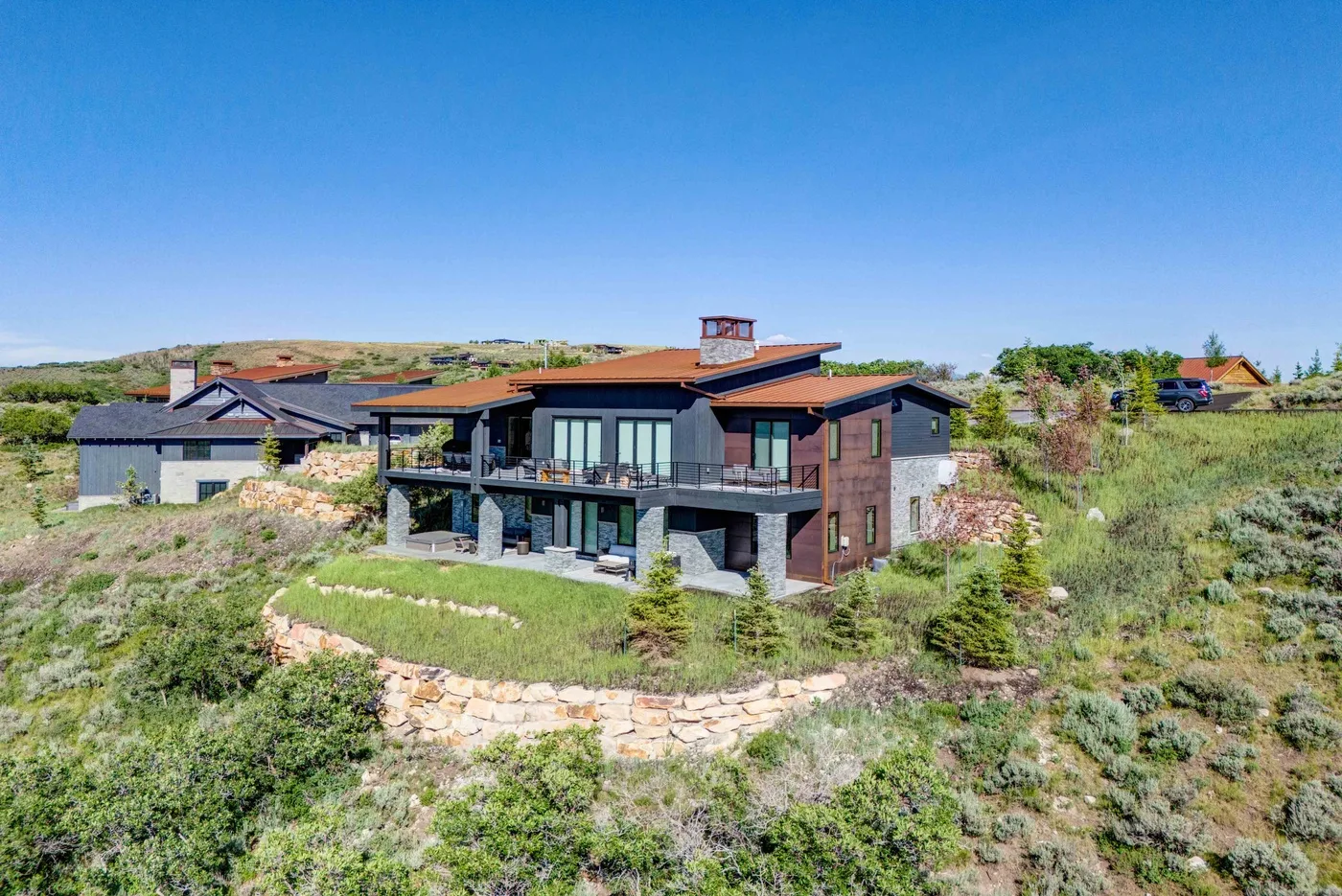 A modern house sits on a grassy hillside beneath a clear blue sky.