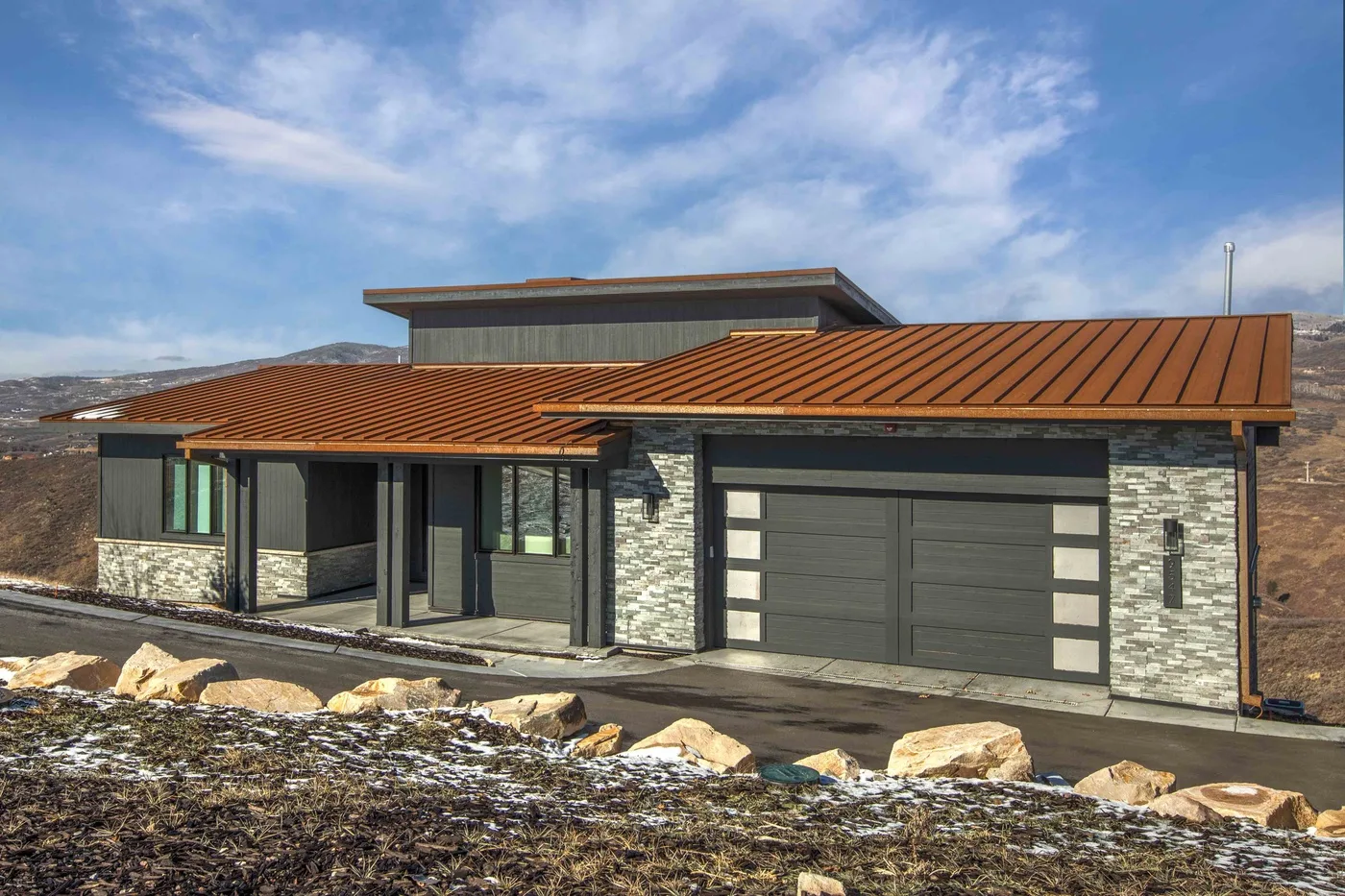 A modern house with stone exterior walls, a red roof, and a large garage door.