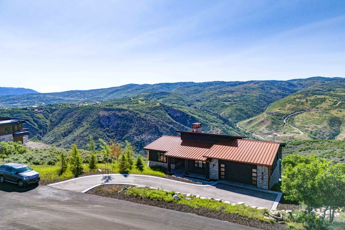 A house with a red roof sits beside a road overlooking green hills.