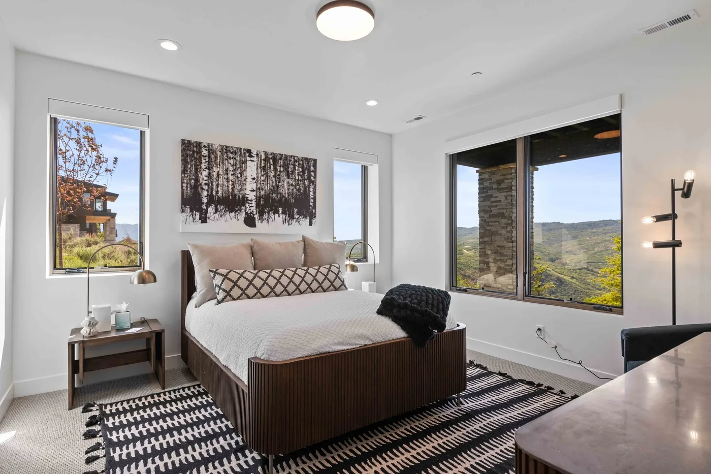 A bright bedroom with a bed facing wide windows overlooking a green landscape.