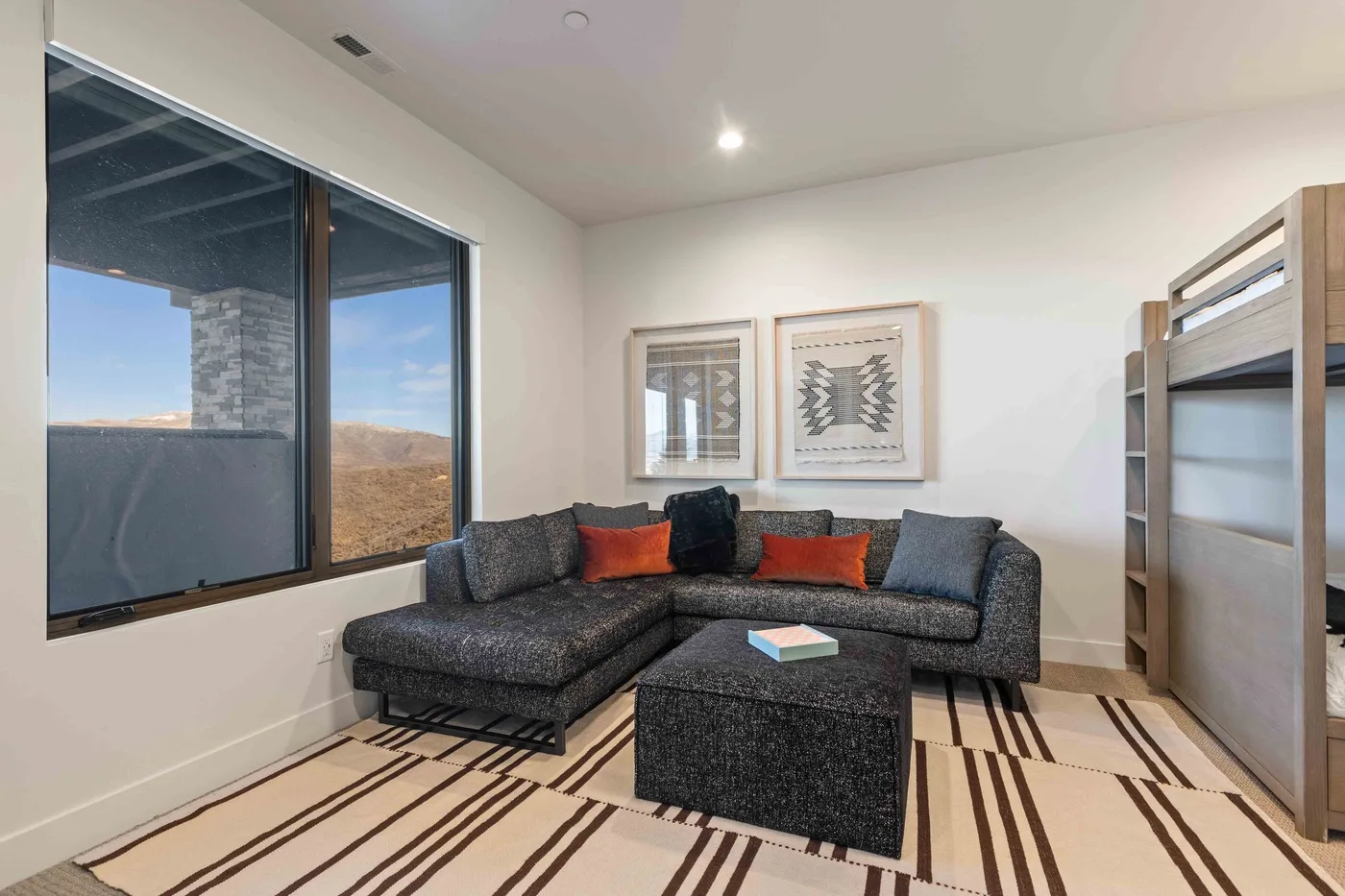 A living room with a dark sectional sofa, matching ottoman, and large windows.