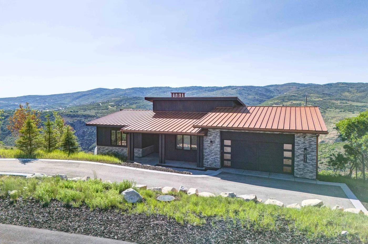 A modern house with a metal roof sits against a backdrop of rolling hills.