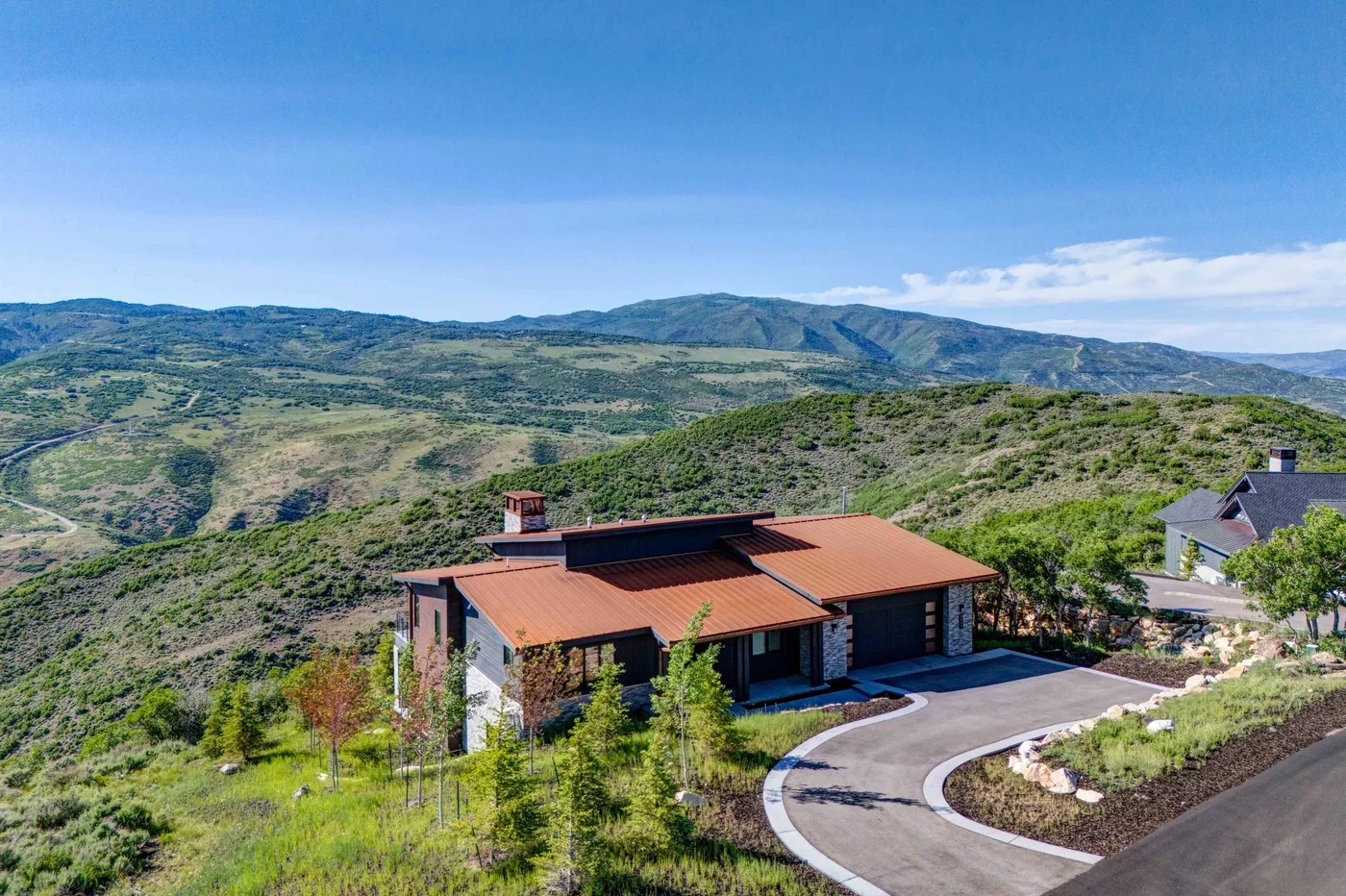 A house with a red roof sits among green hills beside a curving driveway.