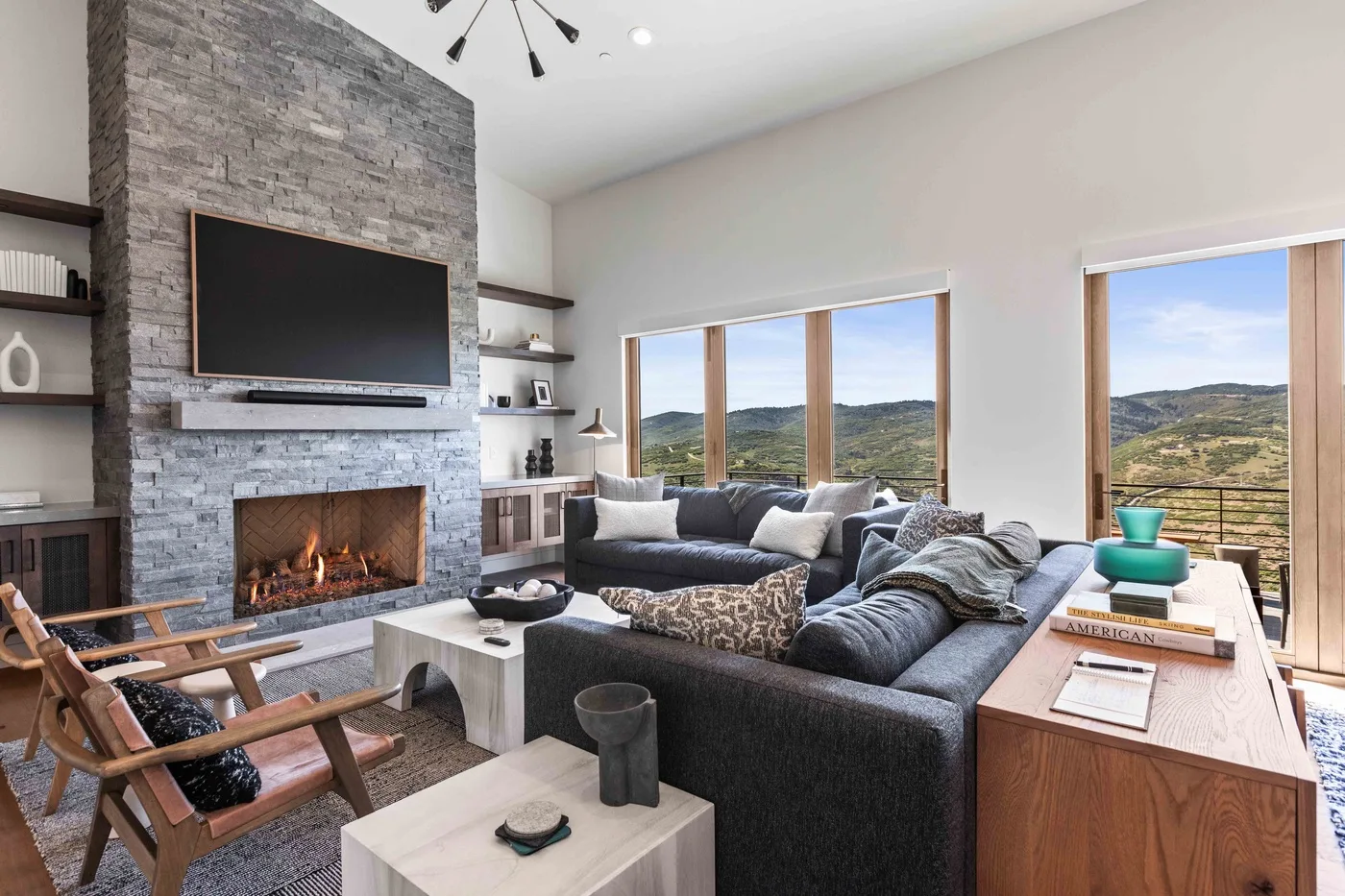 Una luminosa sala de estar con asientos, chimenea y grandes ventanales con vistas a las colinas.