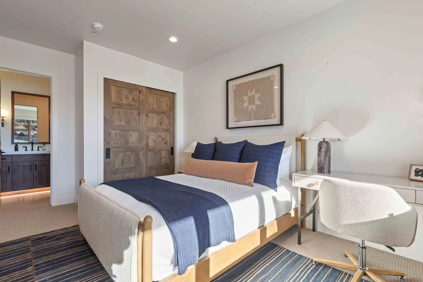 A bright bedroom with a bed dressed in blue bedding and a framed print above it.
