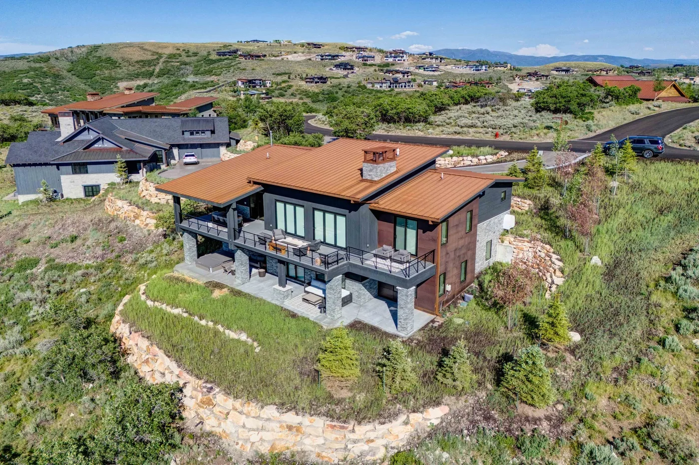 A modern house sits on a landscaped hillside, with other homes across the surrounding hills.