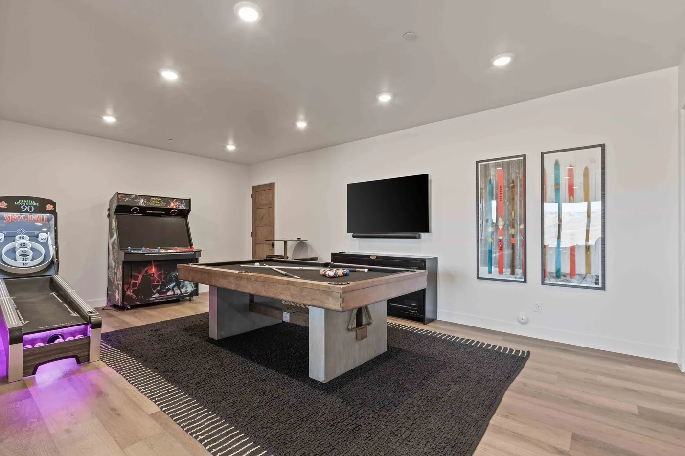 A recreation room with a pool table, arcade games, and a wall-mounted television.