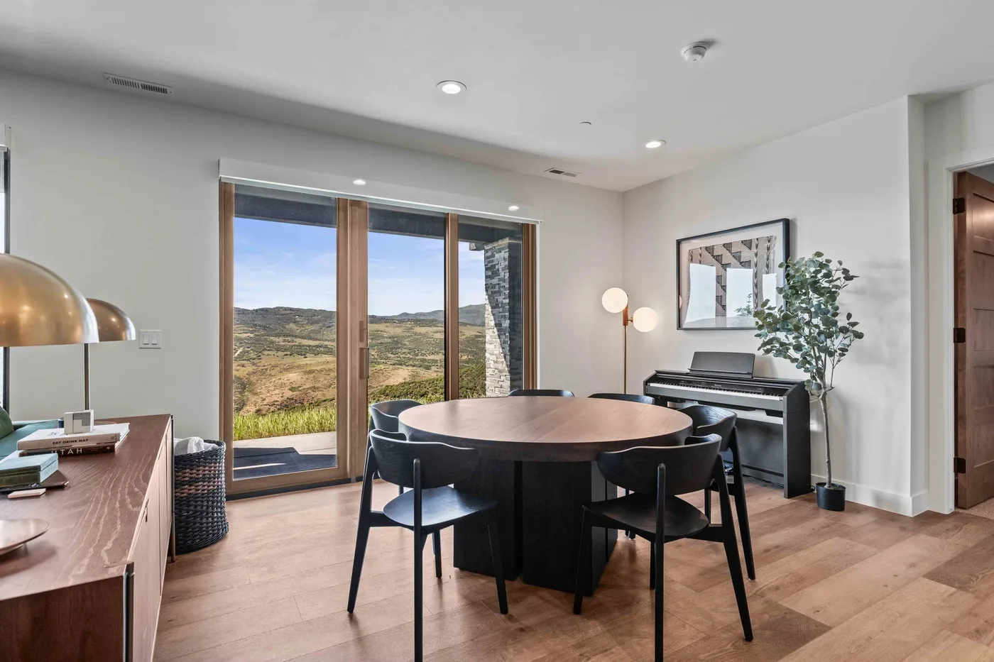 A dining area with a round table and seating beside large windows overlooking the hills.